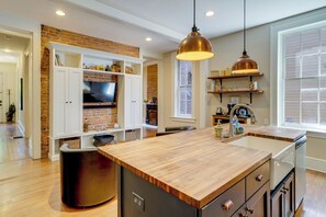 Una cocina con una isla de madera, armarios blancos, una pared de ladrillo decorativa y una lámpara colgante.