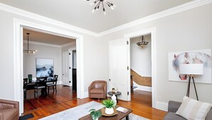 A living room with a sofa, coffee table, and a painting. There is a dining area with a table and chairs.