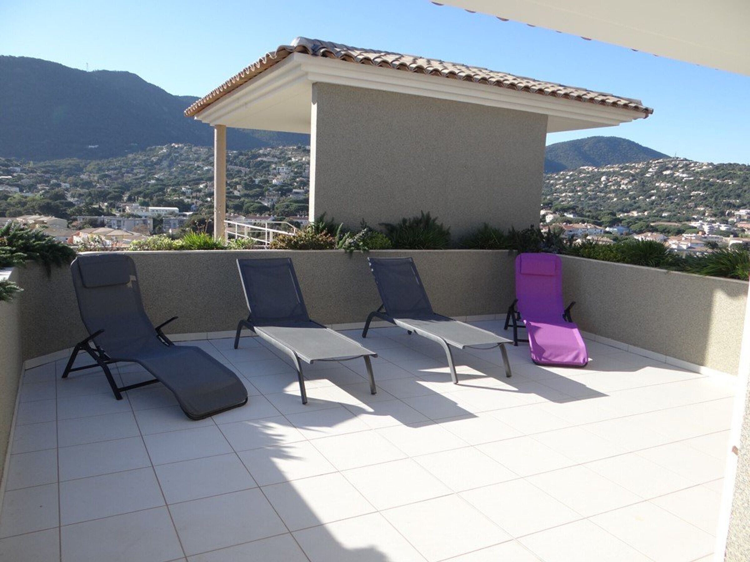 Une terrasse dotée de quatre fauteuils de jardin, d’une pergola et offrant une vue sur un paysage montagneux.