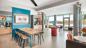 A modern hotel lobby with a wooden reception desk, a large framed logo, and a seating area with tables and chairs. - avid hotel Fresnillo by IHG (Fresnillo)