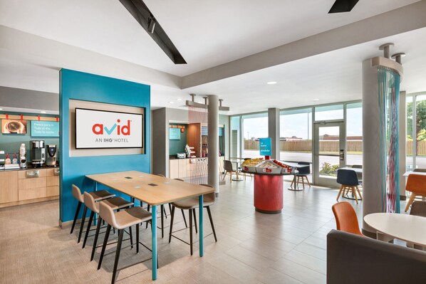 A modern hotel lobby with a wooden reception desk, a large framed logo, and a seating area with tables and chairs.
