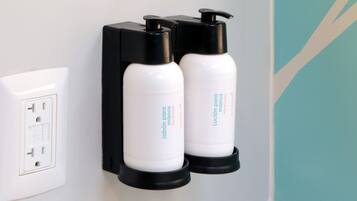 Two white hand soap dispensers mounted on a black holder against a wall with a white electrical outlet.