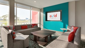 A modern hotel room with a large window, grey sofas with red cushions, a central coffee table, and a teal accent wall with a framed logo. - avid hotel Fresnillo by IHG (Fresnillo)