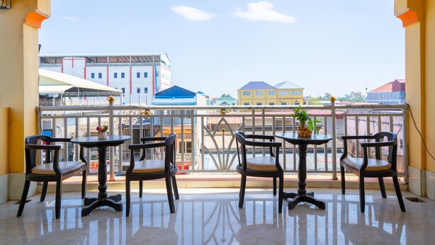 Un balcon avec quatre chaises et une table, d’où l’on peut admirer un paysage urbain avec ses bâtiments et un ciel dégagé.