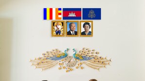 Deux réceptionnistes sont assis derrière un comptoir, avec un paon décoratif et des drapeaux suspendus au-dessus.