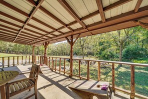 A covered outdoor area with a wooden bench, a table, and a view of a forested area. - Rustic Cabin w/ Hot Tub Near Broken Bow Lake! (Broken Bow)