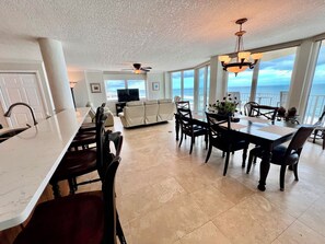 A spacious living area with a large dining table, comfortable seating, a television, and a view of the ocean. - #901 Shores Club Oceanfront 3/3 Traffic Free Beach (Daytona Beach Shores)