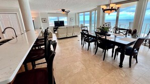 A spacious living area with a large dining table, comfortable seating, a television, and a view of the ocean. - Shores Club Direct Oceanfront 3/3 on Traffic Free Beach - Unit 901 (Daytona Beach Shores)
