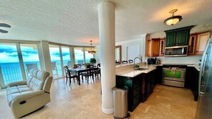 A spacious living area with a balcony overlooking the ocean, a dining area, and a modern kitchen with stainless steel appliances. - Shores Club Direct Oceanfront 3/3 on Traffic Free Beach - Unit 901 (Daytona Beach Shores)