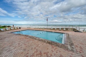 A swimming pool with a view of the ocean, surrounded by lounge chairs and a flag. - Shores Club Direct Oceanfront 3/3 on Traffic Free Beach - Unit 901 (Daytona Beach Shores)