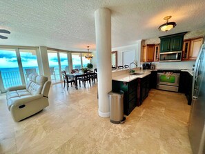 A spacious living area with a balcony overlooking the ocean, a dining area, and a modern kitchen with stainless steel appliances. - #901 Shores Club Oceanfront 3/3 Traffic Free Beach (Daytona Beach Shores)