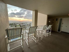 A balcony with white chairs and a table, overlooking a scenic view of a sunset over a coastal town. - #901 Shores Club Oceanfront 3/3 Traffic Free Beach (Daytona Beach Shores)