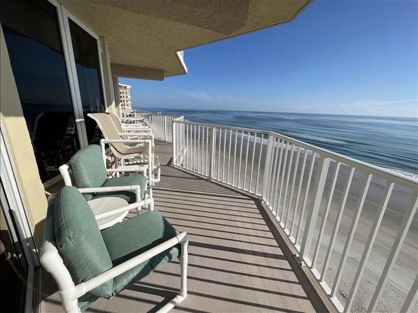 Un balcon avec des balustrades blanches, une rangée de chaises longues blanches et une vue sur l’océan.