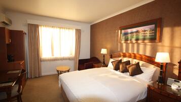 Habitación de hotel con una cama grande, un escritorio, una silla, una mesita y un cuadro en la pared.
