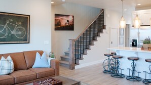 Ein modernes Wohnzimmer mit braunem Sofa, einer Treppe und einer Küchenzeile mit Barhocker.
