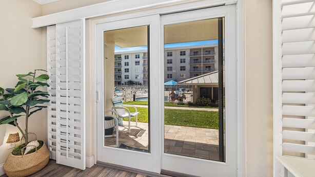 Une porte-fenêtre coulissante donne sur une terrasse extérieure avec une piscine, et on aperçoit un bâtiment au fond.
