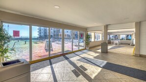 Un espace intérieur vaste et lumineux, doté de grandes fenêtres, d’un sol carrelé et offrant une vue sur un patio extérieur.