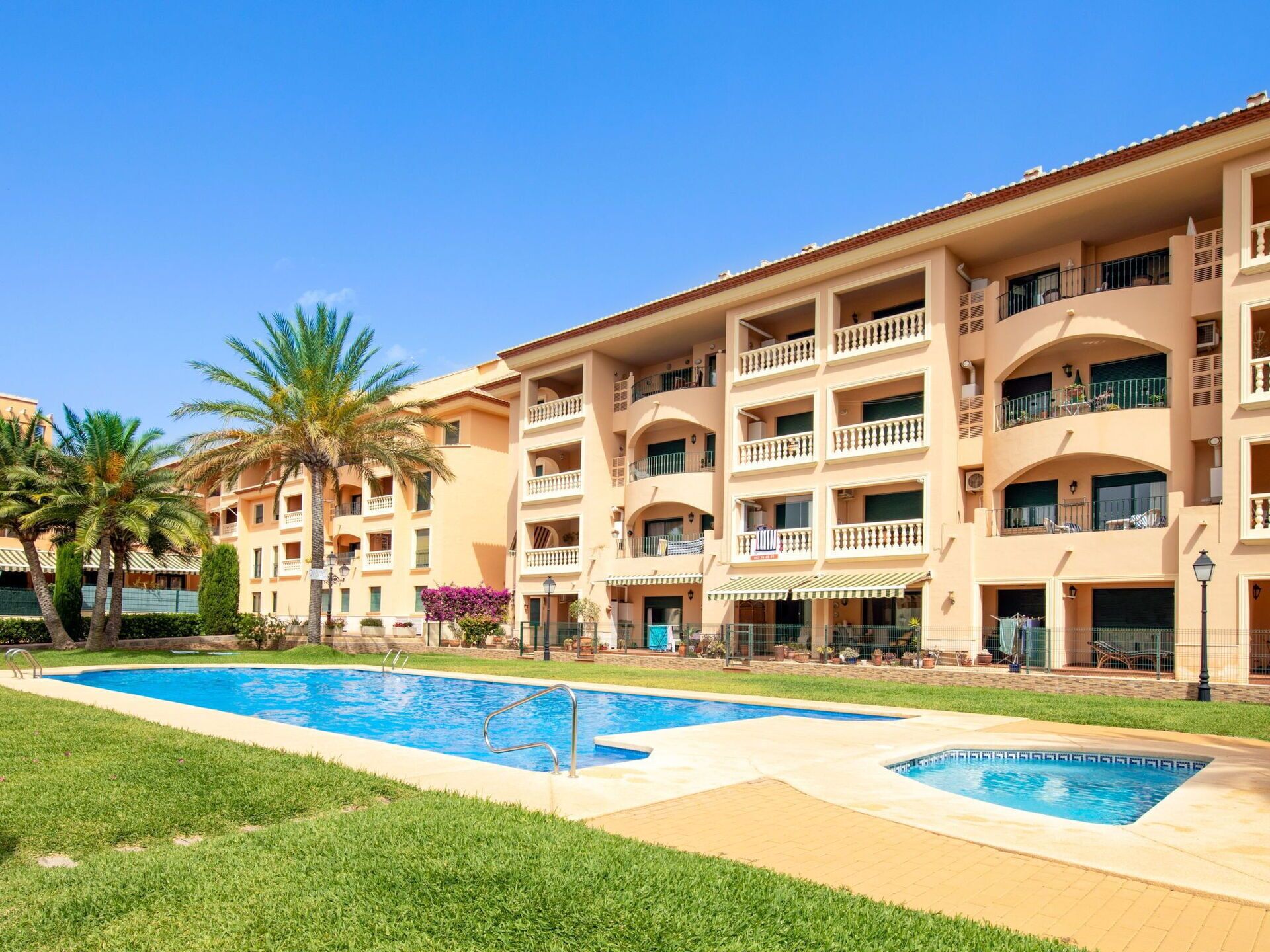 Un hotel con piscina, varios balcones y palmeras.