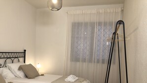 A hotel room with two beds, a bedside table with a lamp, a window with sheer curtains, and a wooden ladder against the wall. - Casa a La Pera 4/6 pax - Costa Brava (La Pera)