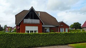 Une maison à deux étages avec une façade en briques rouges, une porte de garage blanche et un petit balcon agrémenté d’une balustrade blanche.