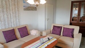 Un salon avec deux canapés beige, chacun agrémenté d’un coussin violet, d’un chemin de table à rayures, d’un vase en verre et d’une télécommande.