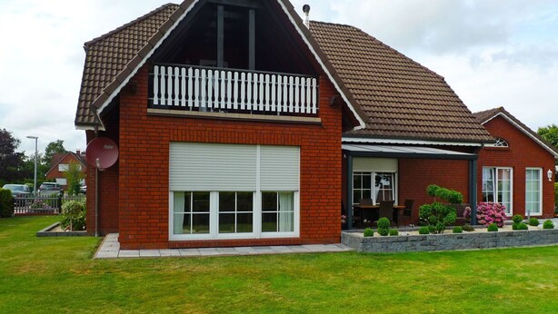 Une maison à deux étages avec une façade en briques rouges, une porte de garage blanche et un petit balcon doté d’une balustrade blanche.