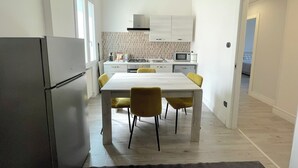A modern kitchen with white cabinets, a dining table with yellow chairs, and a refrigerator. - At the sight of the Baroque  (Lecce)