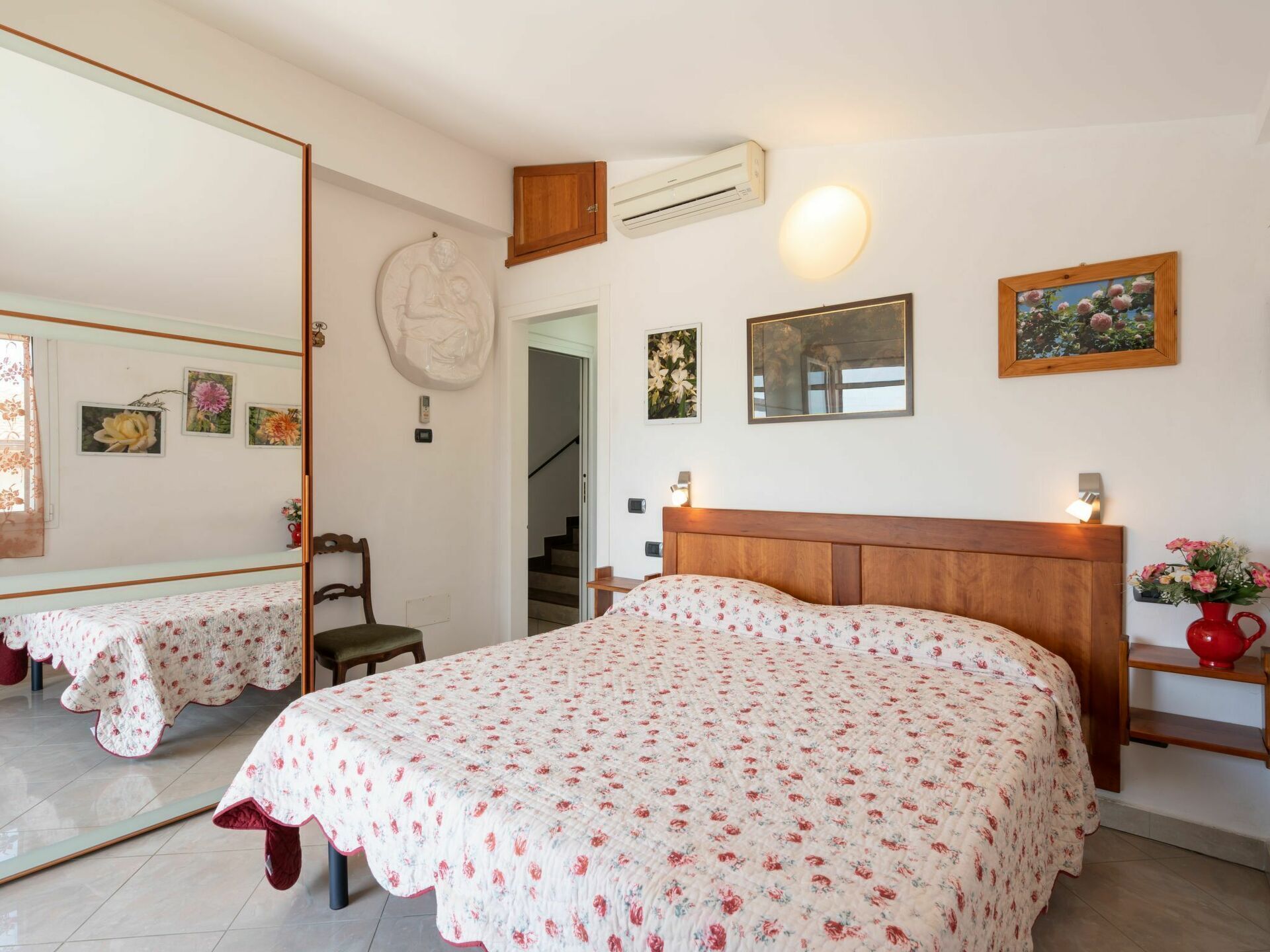 Un dormitorio con cama, cabecera de madera, espejo, aire acondicionado de pared y una escalera que lleva a otra habitación.