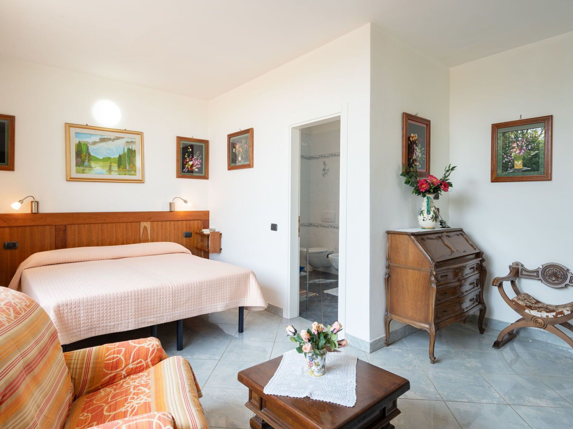 A bedroom with a bed, a dresser, a chair, and a small table with a vase of flowers.