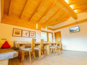 Uma sala de jantar acolhedora com mobiliário de madeira, uma TV na parede e quadros decorativos.