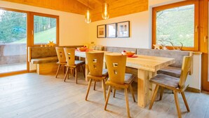 Zona pranzo con tavolo e sedie in legno, ampie finestre e soffitto in legno.