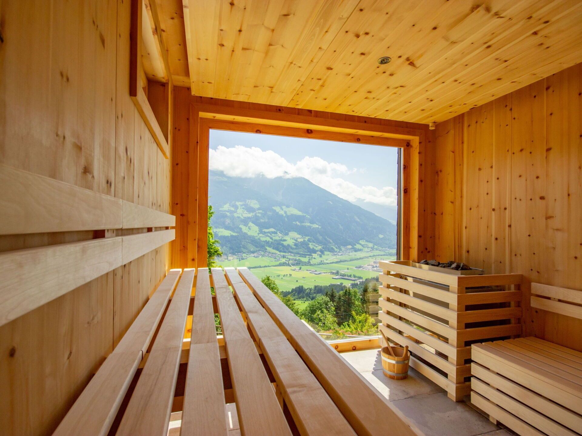 Een houten sauna met banken en uitzicht op een bergachtig landschap.