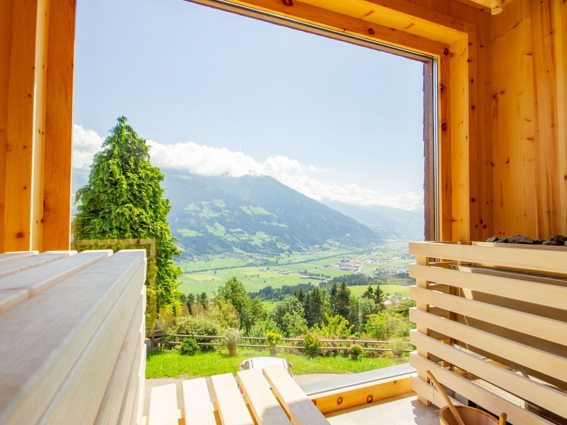 A wooden cabin with a large window overlooking a valley and mountains.
