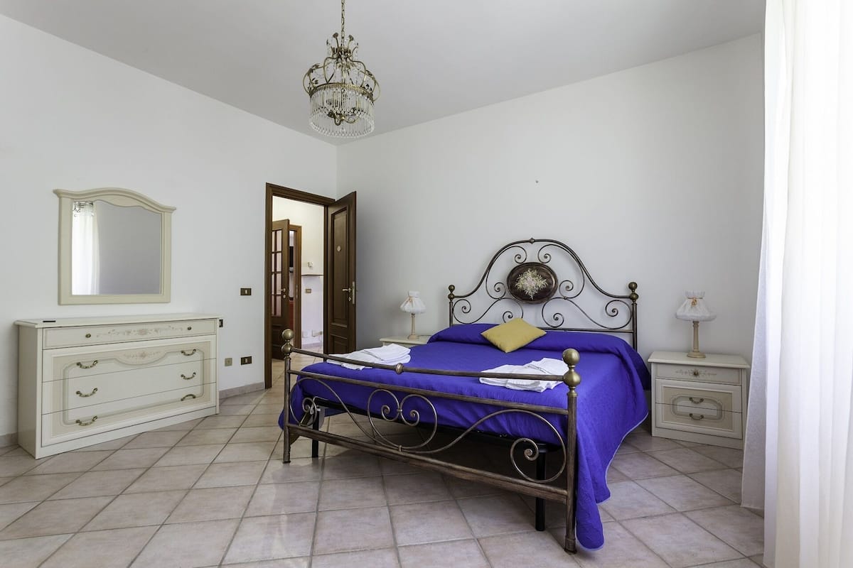 A bedroom with a bed, a dresser, a mirror, and a chandelier.