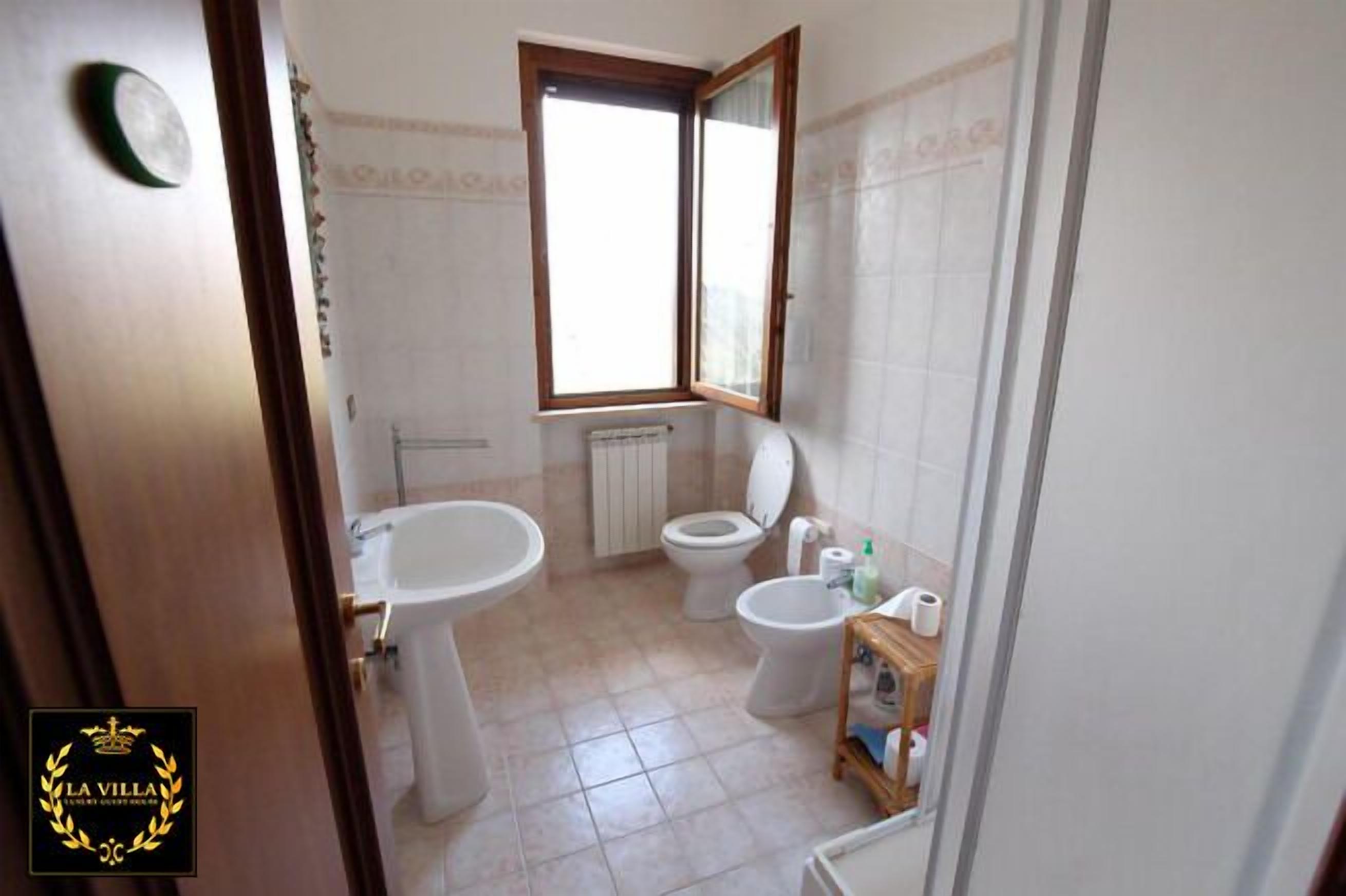Un baño con lavamanos pedestal, dos inodoros, una ventana y un radiador.