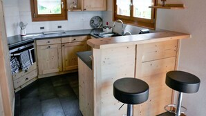 A kitchen with wooden cabinets, a sink, and two bar stools. - Lovely apartment in villa for 6 guests with WIFI, TV and terrace (Basse-nendaz)