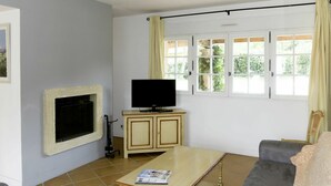 A living room with a television on a wooden cabinet, a coffee table with a magazine, and a couch. - Beautiful apartment in villa for 8 people with A/C, WIFI, pool, TV, terrace and pets allowed (Les Saquetons)