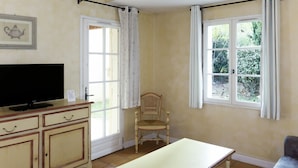 A room with a television on a cabinet, a wooden chair, a table, and two windows with curtains. - Lovely apartment in villa for 4 guests with A/C, pool, WIFI, TV, patio and pets allowed (Les Saquetons)