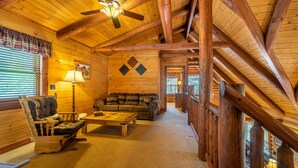 Ein Holzblockhaus-Interieur mit Holzbalkendecke, Deckenventilator, einer Couch, einem Schaukelstuhl und einer Lampe.