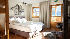 Un dormitorio con cama, una silla de madera, un perro y una ventana con cortinas.