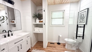Un baño con muebles blancos, un espejo, un lavabo, un inodoro y una zona de ducha.