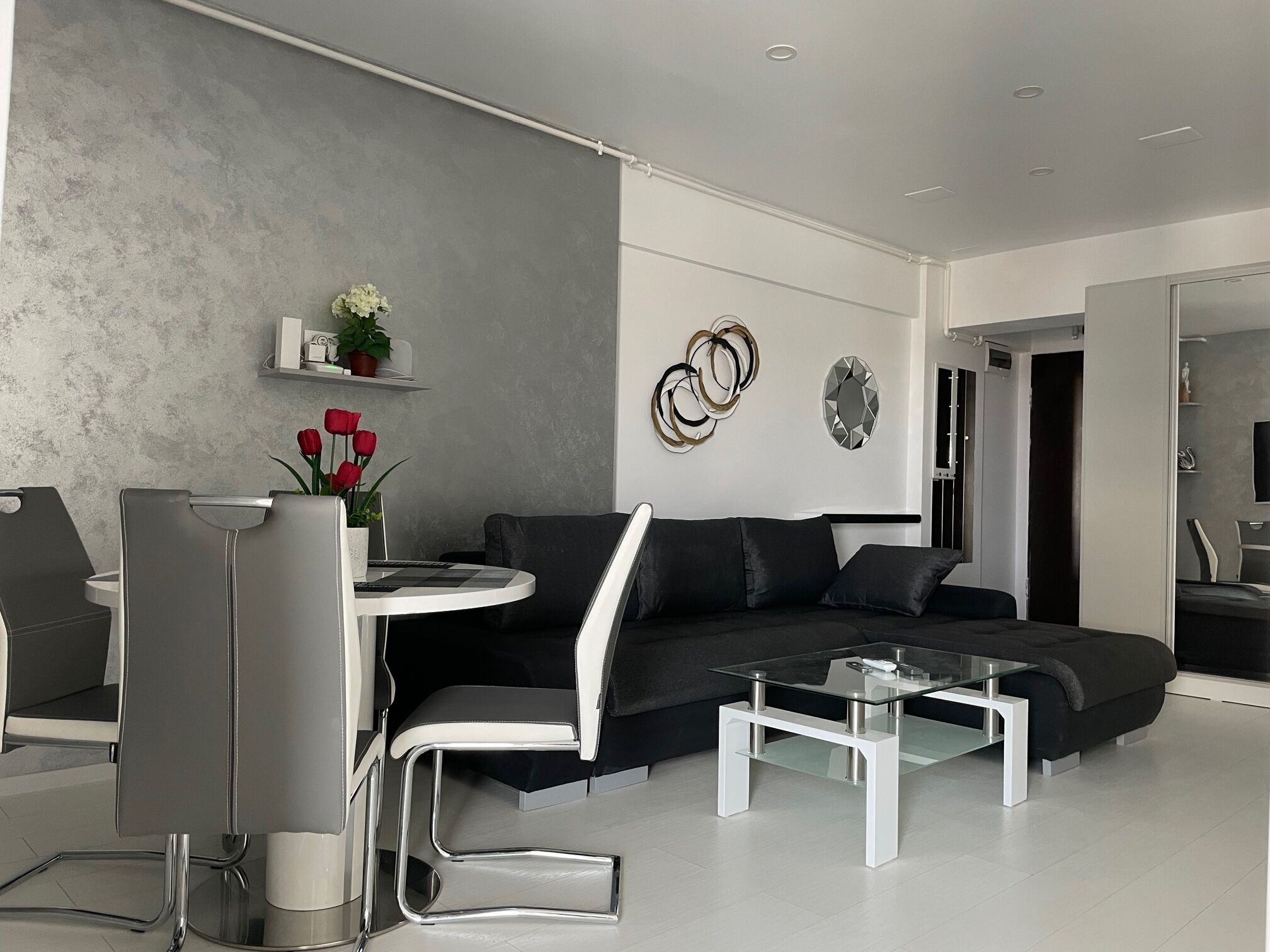 A modern living room with a grey sofa, a glass coffee table, and a dining area with a white table and chairs.