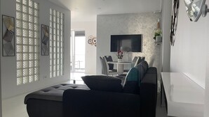 A modern living room with a dark sofa, a dining area with a glass table, and a TV mounted on the wall. - Westpark2 One-Bedroom Suite W5 Lakeview (Bucharest)