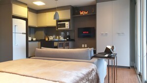 Una habitación de hotel moderna con una cama grande, kitchenette, televisor de pantalla plana y un letrero que dice 'Wow'.