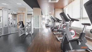 Un gimnasio con equipo de ejercicio, piso de madera y ventanas amplias.