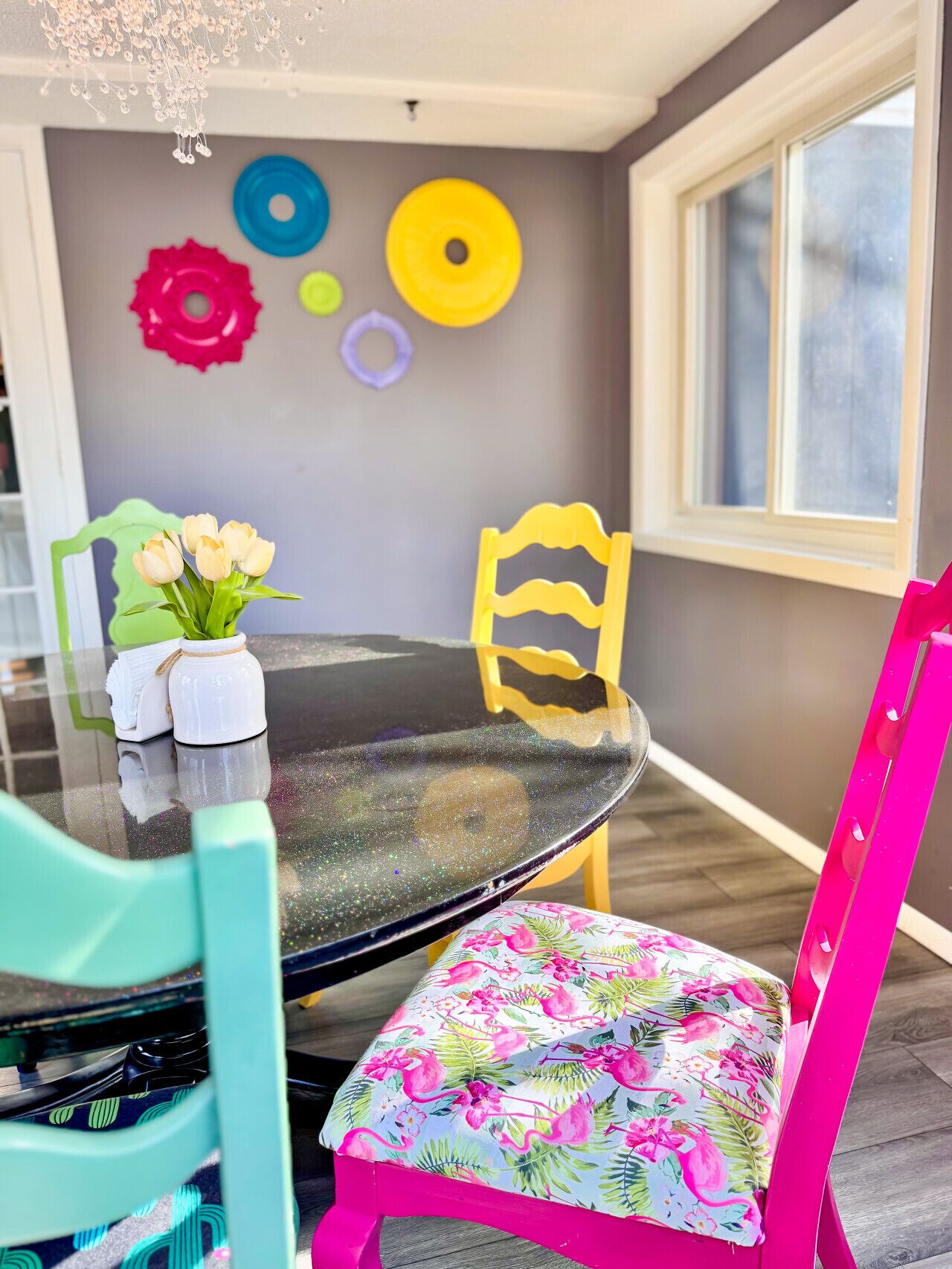 A dining area with a round glass table, teal chairs, and a vibrant floral chair cushion.