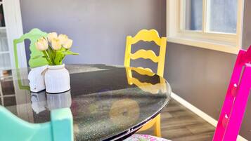 A dining area with a round glass table, teal chairs, and a vibrant floral chair cushion.