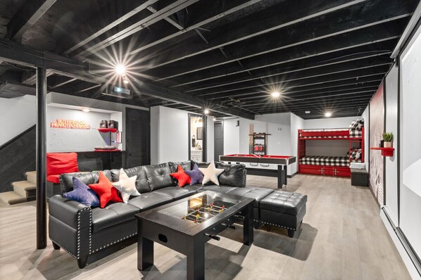 A modern living room with a leather sofa, a pool table, and a red bunk bed.