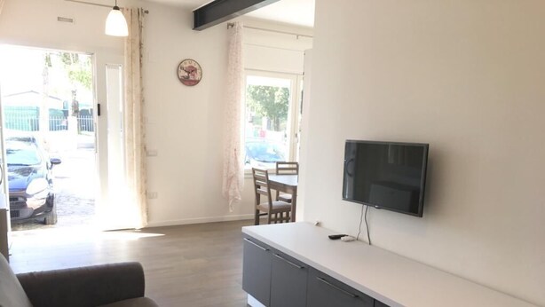 Ein modernes Wohnzimmer mit einer Couch, einem an der Wand montierten Fernseher und einer Küchenzeile mit Schränken.