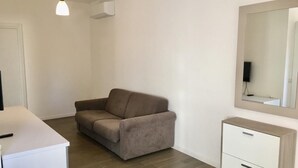 Ein moderner, minimalistischer Raum mit einem braunen Sofa, einem weißen Schreibtisch und einem kleinen Schrank.
